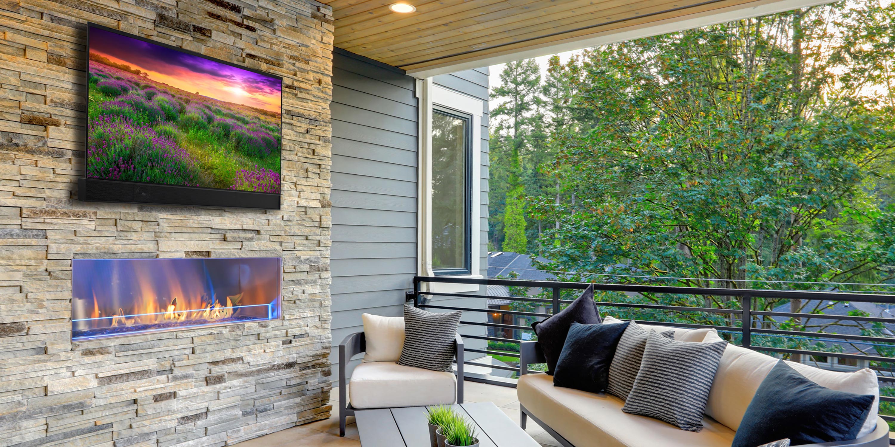 Cozy outdoor patio with stone fireplace, mounted TV, and cushioned seating