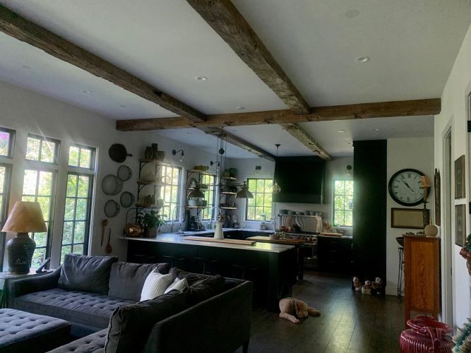 Wider view of kitchen and living space with dark cabinetry and large wall clock