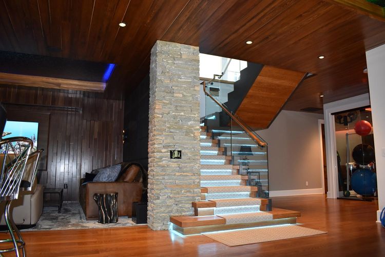 Illuminated staircase with glass railing, next to stone column and lounge area