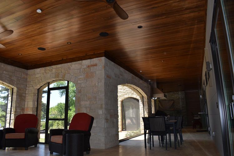Covered patio dining space with arched stone walls and glass doors to interior