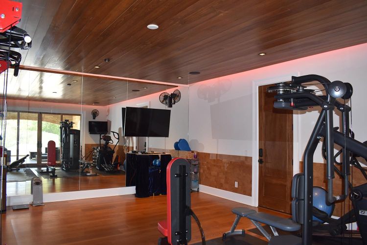 Home gym with mirrored wall, mounted TV, and wood-paneled ceiling