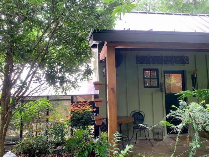 Small porch with chairs, potted plants, and shaded trees surrounding it