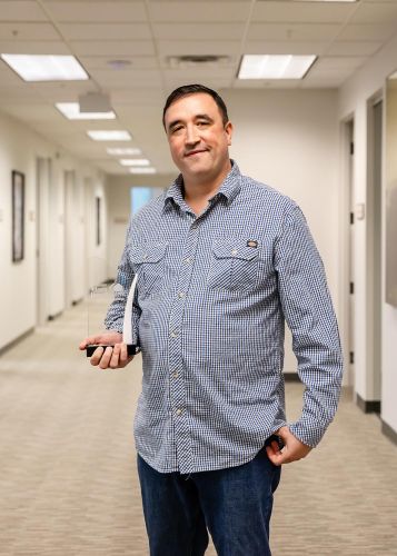 Man smiling and holding an award in a well-lit office hallway