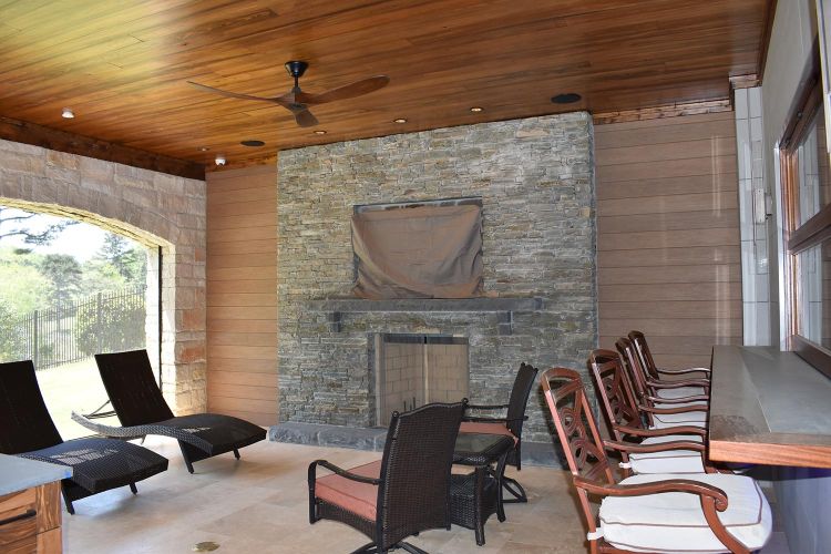 Covered patio with stone fireplace, cushioned seating, and wood plank ceiling