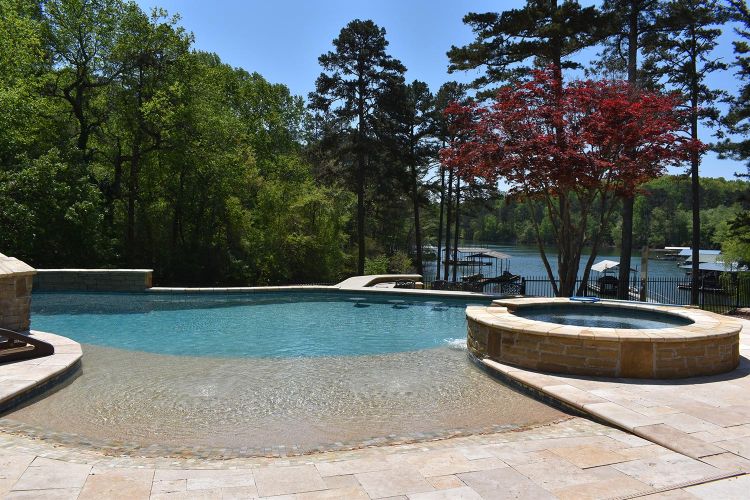 Infinity-edge pool with hot tub overlooking a wooded lakefront and boat docks