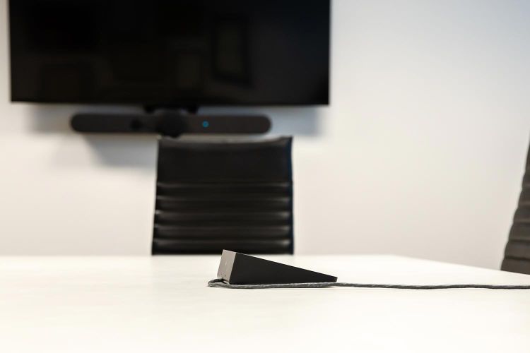 Close-up of conference table speakerphone with screen in background