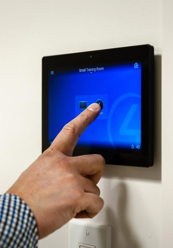 Hand pressing touchscreen wall panel labeled “Small Training Room”