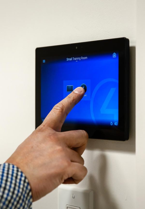 Hand pressing touchscreen wall panel labeled “Small Training Room”