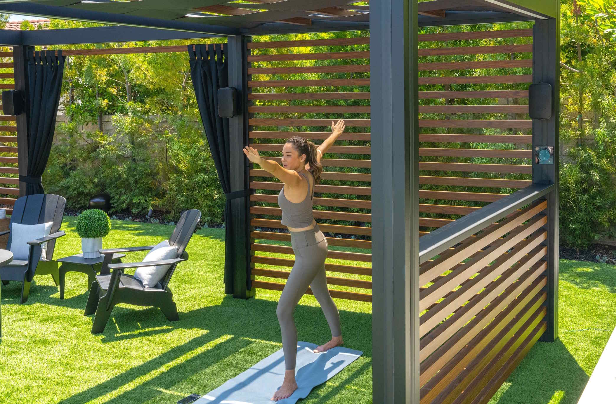 Outdoor pergola space with a person stretching on a yoga mat surrounded by greenery.